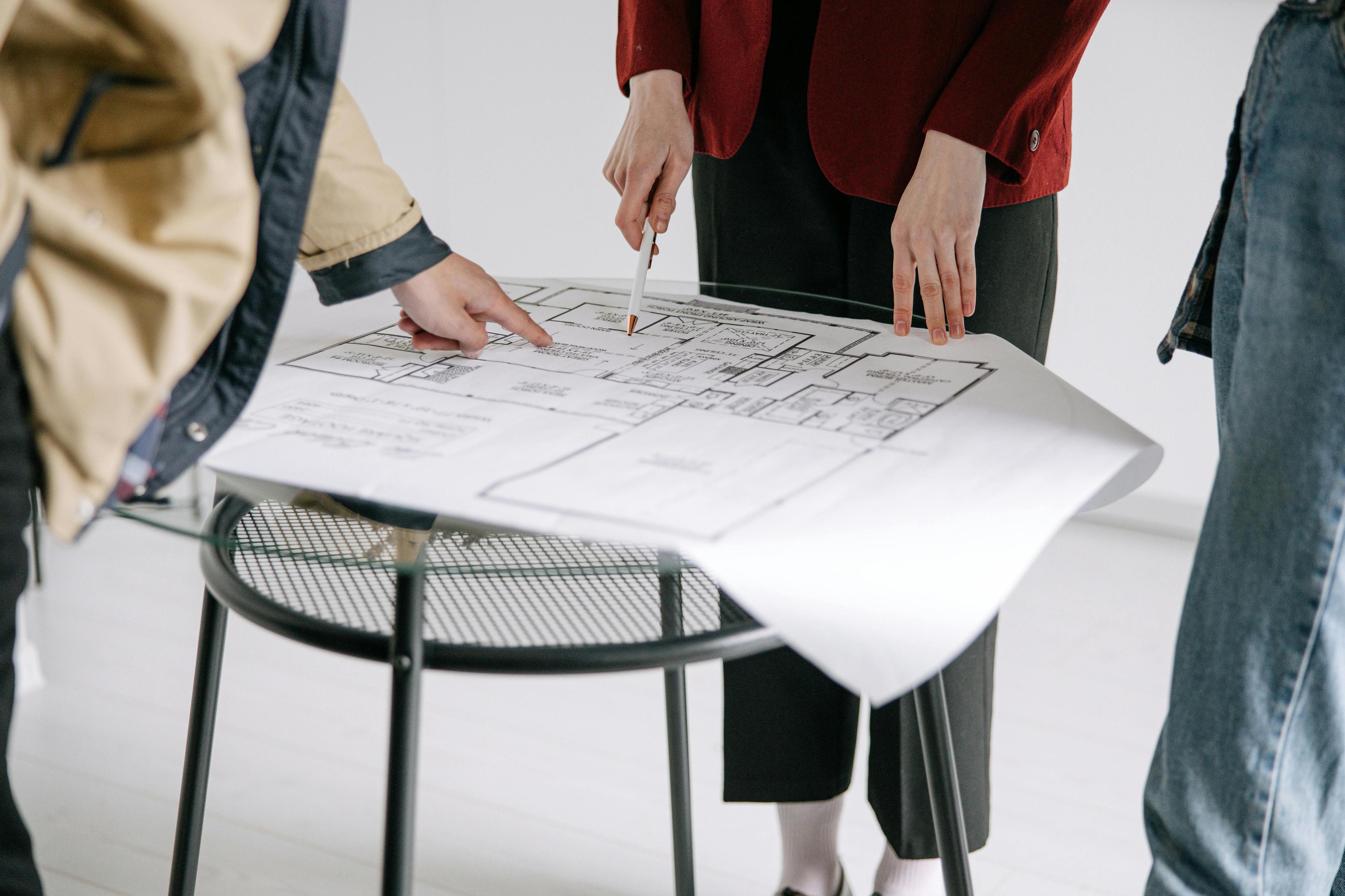 Personnes discutant d'un plan architectural sur une table ronde, collaboration en architecture d'intérieur et conception de projet.